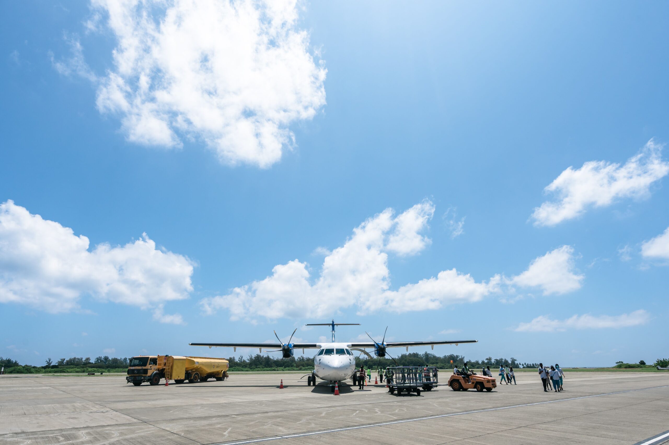 Airplane parked on airport tarmac with crew under a sunny sky.